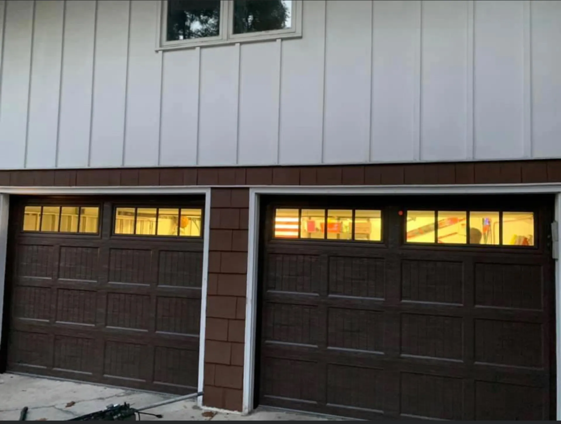 Dark brown carriage-style garage doors with lit interior windows at dusk