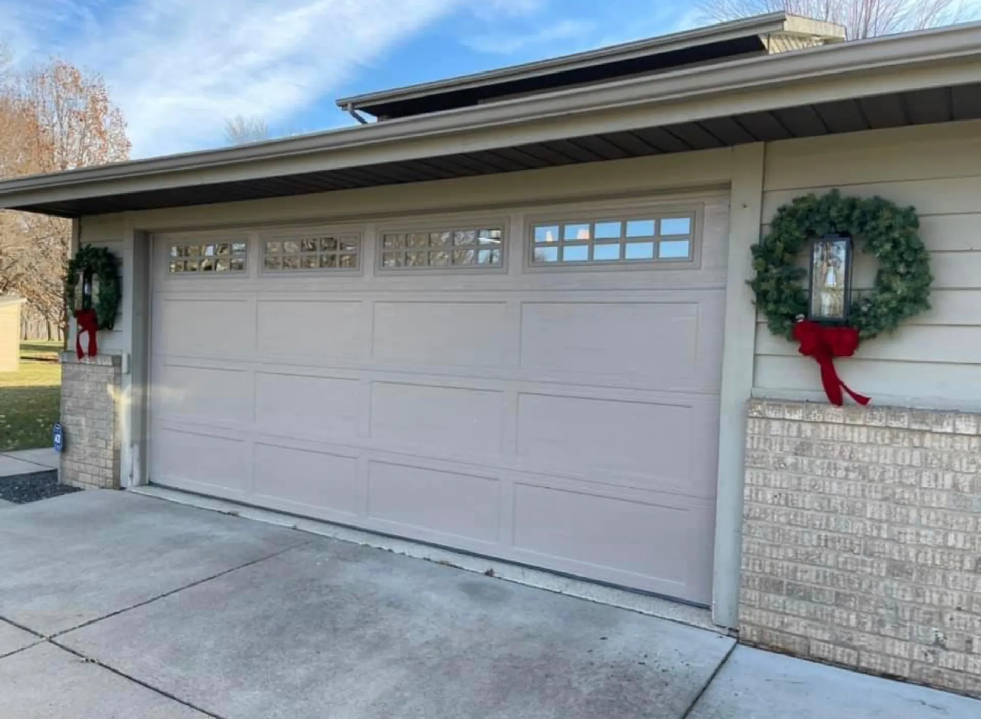 Tan carriage-style garage door decorated with wreaths for the holidays