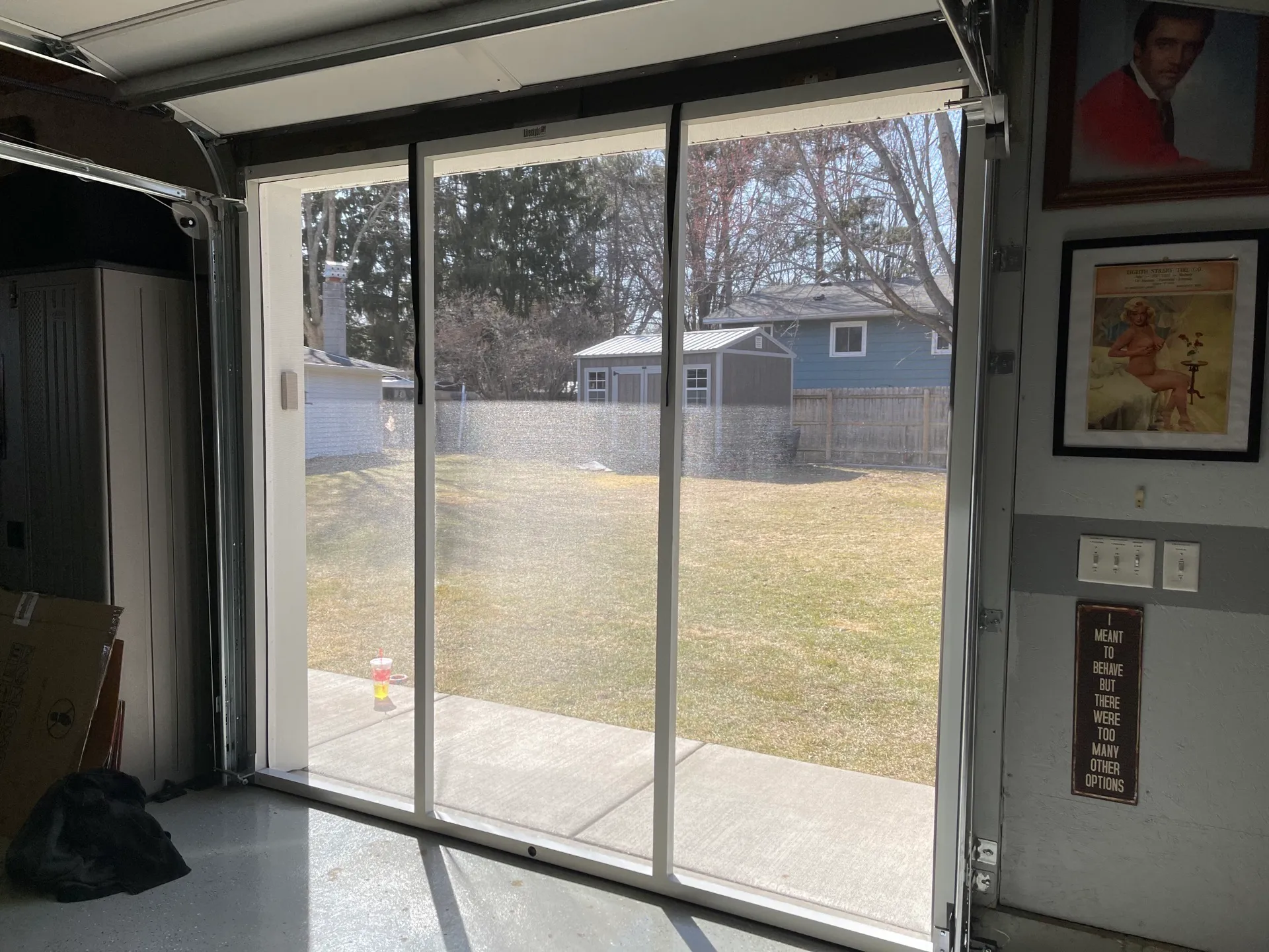 Inside a garage looking out through a Lifestyle Screen to a sunlit backyard